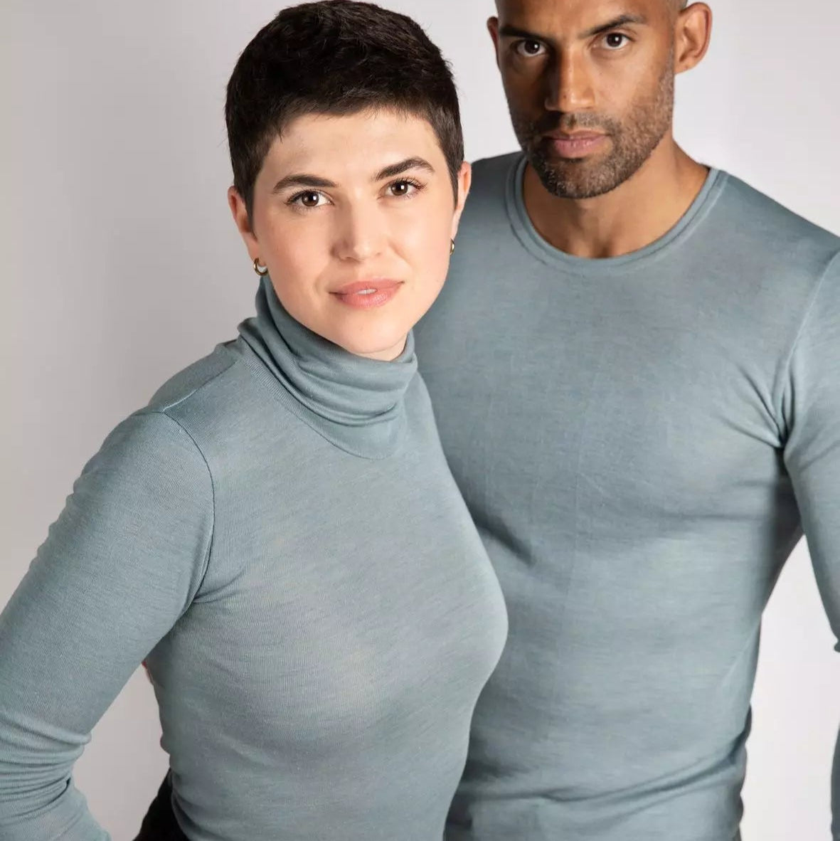 Two people wearing matching light gray long-sleeve shirts against a plain background