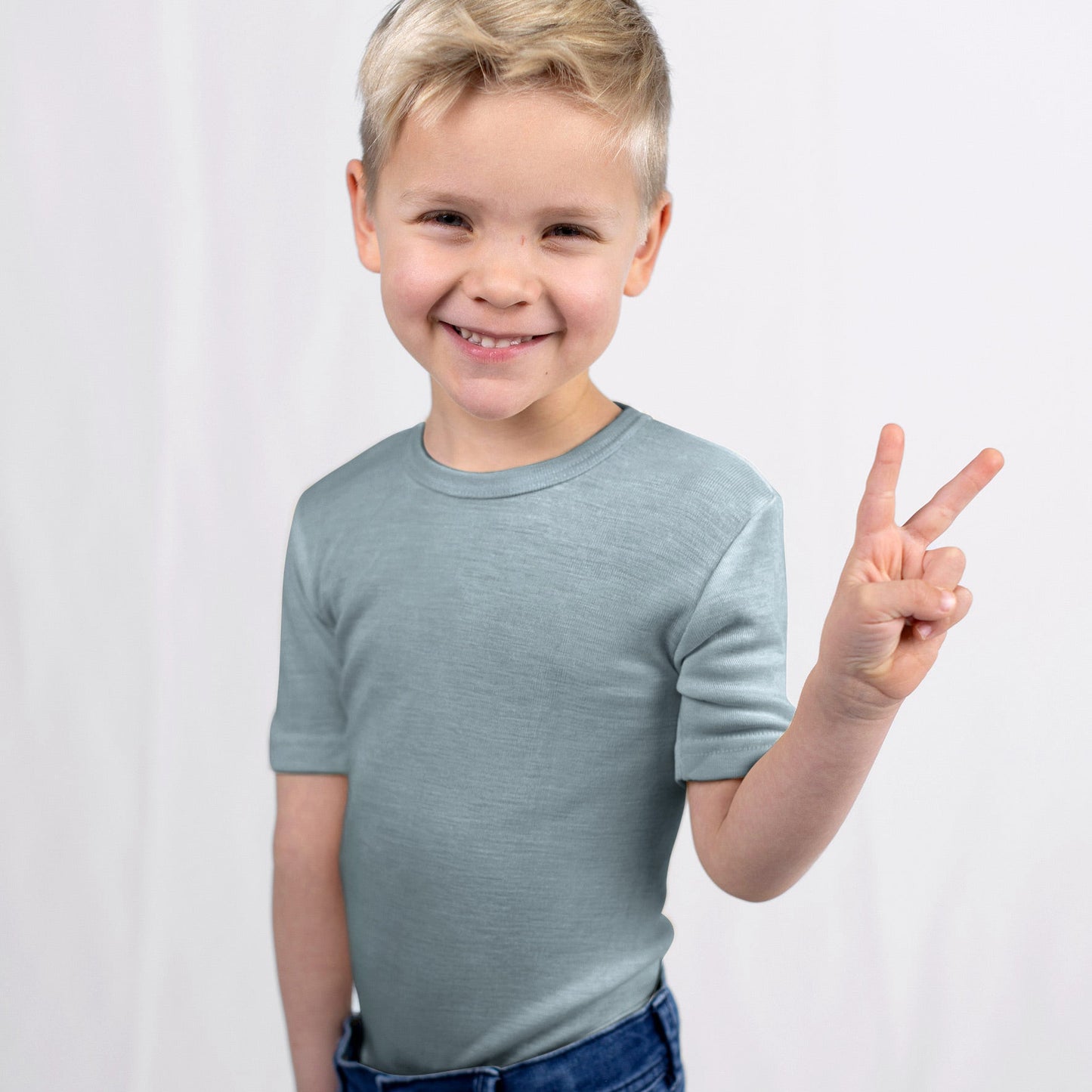 Child wearing a light blue shirt and dark blue jeans, making a peace sign on a white background